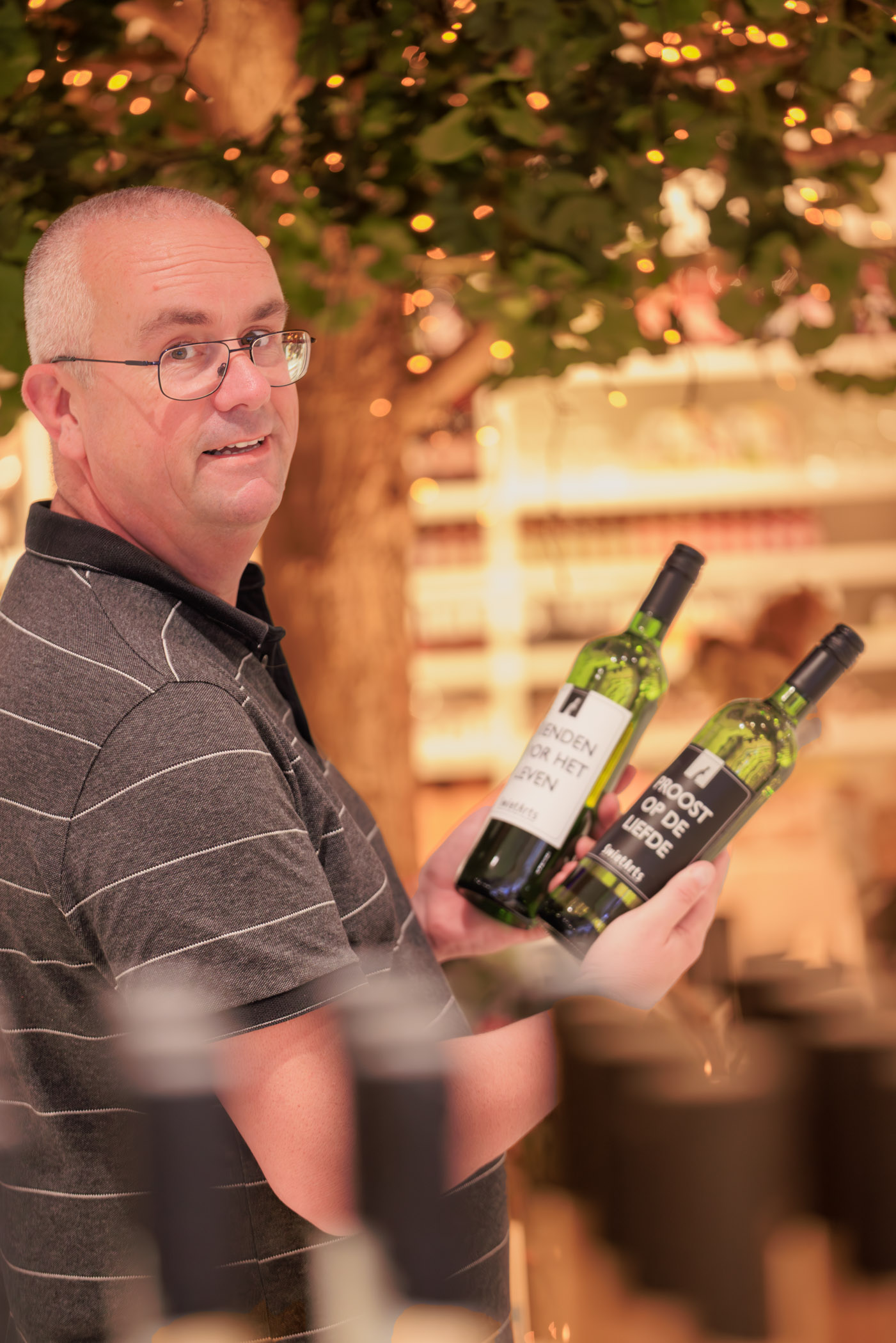 Foto van Patrick, eigenaar van de winkel SwietArts in Hoogvliet. Met gepersonaliseerde wijnflessen van eigen label